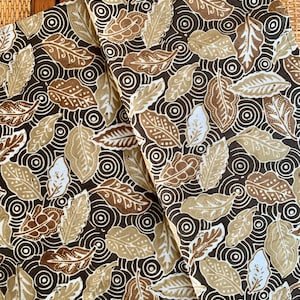 Könnte beinhalten: Ein brauner Stoff mit einem Muster aus weißen und braunen Blättern auf einem dunkelbraunen Hintergrund. Die Blätter sind in einem sich wiederholenden Muster angeordnet und von kleinen Kreisen umgeben.