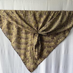 Peut inclure: Un foulard triangulaire avec un motif répétitif de feuilles brun foncé et vert olive. Le tissu présente une bordure brun foncé et une petite étiquette rectangulaire attachée au coin supérieur gauche avec le texte The Collection of L.L. Bean.