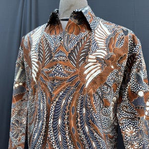 Peut inclure: Une chemise à manches longues avec un motif floral brun, blanc et bleu. Le motif représente un grand oiseau aux ailes déployées.