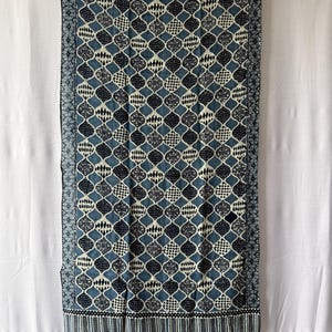 Peut inclure: Un chemin de table rectangulaire en tissu présentant un motif répétitif de formes ogivales bleu foncé et crème. Chaque forme contient des motifs géométriques et pointillés complexes. Les bords sont encadrés par une bordure rayée bleu foncé.