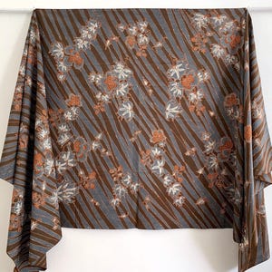 Könnte beinhalten: Ein brauner und blauer Stoff mit einem Blumenmuster. Der Stoff hat ein diagonales Streifenmuster und weiße und orangefarbene Blumen.