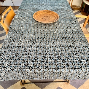 Może przedstawiać: Czarno-niebieski obrus w wzory z plecionym drewnianym tacem w środku. Obrus leży na drewnianym stole z czterema krzesłami.