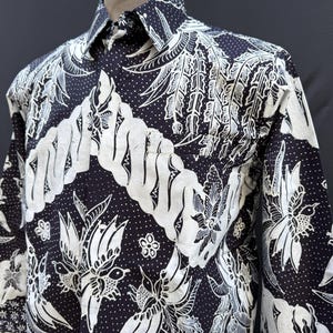 May include: Black and white long-sleeved shirt with a traditional batik pattern. The pattern features intricate floral designs and swirling lines.