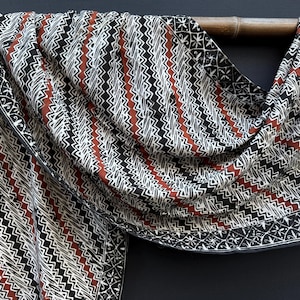 Peut inclure: Un textile rectangulaire présentant un motif répétitif de lignes verticales en zigzag noires, blanches et rouge terre cuite. Le tissu comprend une bordure décorative avec un motif floral blanc sur fond noir, drapé sur une tige en bois.
