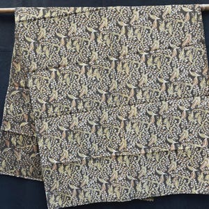 Puede incluir: Una tela plegada con un patrón repetido de hojas y bayas en dorado, beige y rojo sobre un fondo marrón oscuro. La tela está drapeada sobre una varilla de madera, mostrando el intrincado diseño y la textura. Ideal para la decoración del hogar.