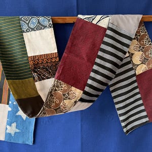 Peut inclure: Un chemin de table patchwork rectangulaire et long composé de divers panneaux de tissu. Le motif comprend des sections à rayures vertes et dorées, bleu avec des étoiles blanches, rayures noires et blanches, bordeaux uni et tissu marron à motifs.