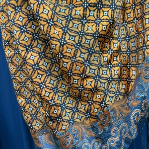 May include: A brown and black patterned silk scarf with a blue and white floral border. The scarf has a fringe on the bottom edge.