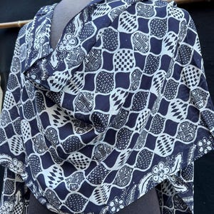 Peut inclure: Écharpe à motifs bleu marine et blancs, drapée sur un mannequin. Le motif géométrique se répète avec des accents floraux. Le tissu léger semble adapté aux températures plus chaudes. Un accessoire polyvalent.