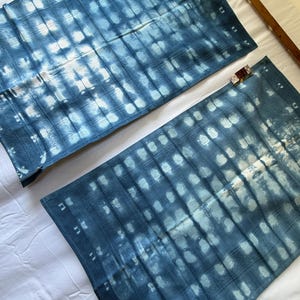 May include: Two rectangular textile pieces featuring a deep blue and white tie-dye pattern. The fabric displays a grid-like arrangement of white rectangular shapes against a dark blue background, with a textured surface and a small tag attached.