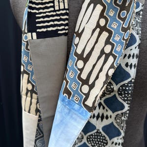 Peut inclure: Une longue écharpe en patchwork avec une variété de motifs géométriques bleus, blancs et noirs. L'écharpe est faite de différents tissus et textures, créant un look unique et intéressant.