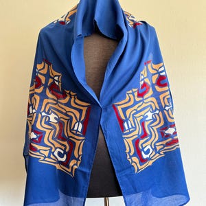 May include: A blue silk scarf with a geometric pattern in shades of red, white, and gold. The pattern is a repeating design of interlocking shapes.