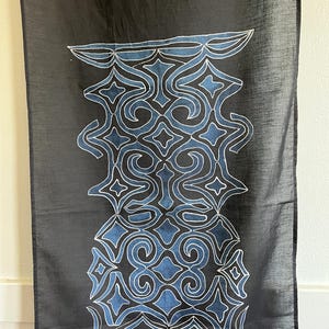 May include: A black fabric wall hanging with a blue and white geometric design. The design is a repeating pattern of swirls and diamonds.