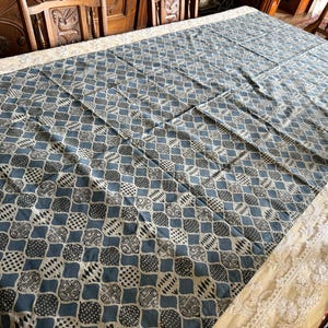 May include: A rectangular tablecloth featuring a repeating pattern of blue and white geometric shapes. The design consists of interconnected ogee-like forms filled with various black and white patterns, including dots, stripes, and cross-hatching.
