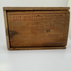 May include: A weathered wooden box with the text "SALT BONELESS CODFISH" and "HALIFAX BRAND" in red lettering. The box also features a graphic of a sailboat and the text "ONE POUND".