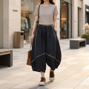 May include: A person wearing a striped top and dark denim culottes with yellow stitching. The culottes have a wide, balloon-like shape. They are carrying a brown tote bag and wearing brown and white trainers.
