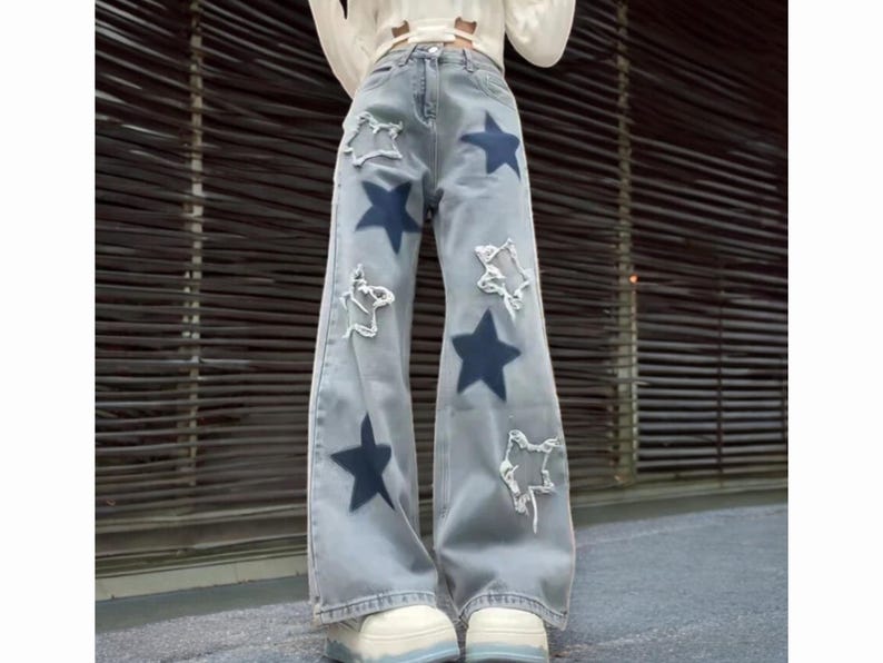 May include: Light blue denim jeans with a wide leg and star-shaped patches. The jeans have a distressed look with frayed edges.