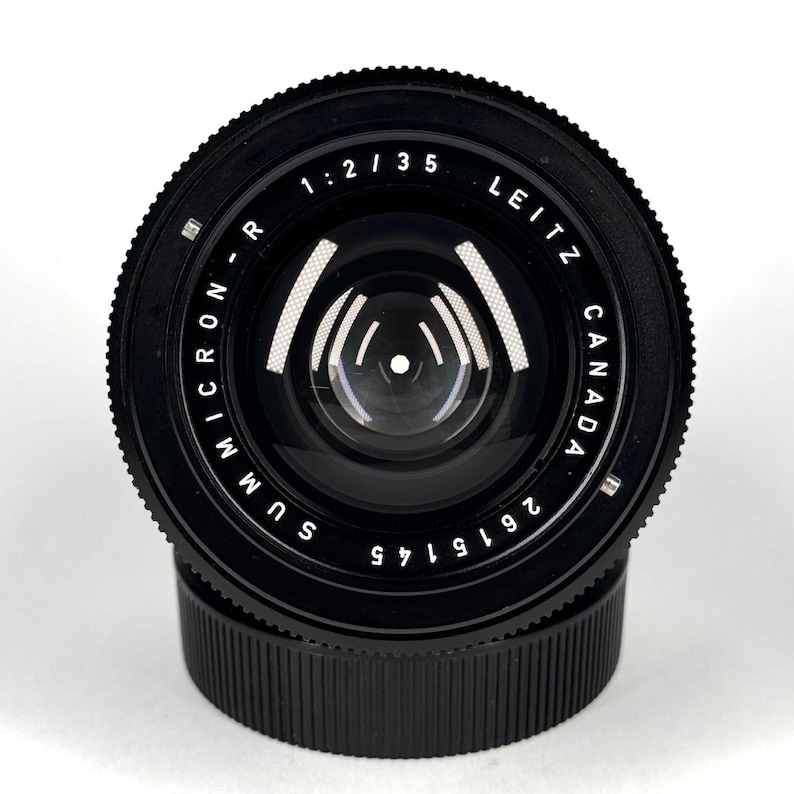 May include: A black Leitz Canada Summicron-R 1:2/35 camera lens with a textured focus ring and a smooth front element. The lens barrel features white engraved text reading Summicron-R, 1:2/35, Leitz Canada, and the serial number 2615145.