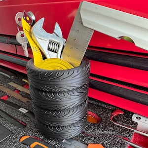 May include: A black tire organizer with a yellow tape measure, a wrench, and a ruler inside. The organizer is sitting on a red toolbox.