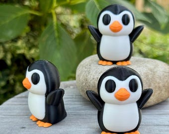 May include: Three small penguin figurines. Each penguin has a black body, white belly, orange beak and feet, and large black eyes. One penguin is turned to the side, while the other two face forward with their arms outstretched.