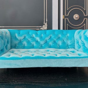 May include: A turquoise blue velvet tufted sofa with a classic design. The sofa has a tufted back and seat, and wooden legs.