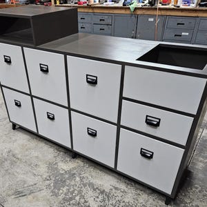 May include: A white cabinet with eight drawers and black handles. The cabinet has a dark grey countertop with a small sink.