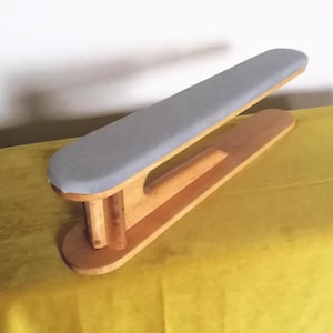 Può includere: Un'asse da stiro in legno con una superficie di stiratura imbottita grigia. L'asse è realizzata in legno chiaro e ha un design curvo. L'asse misura circa 51 cm di lunghezza.