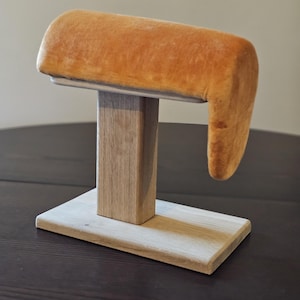 Könnte beinhalten: Ein Holzständer mit einer gepolsterten orangefarbenen Armlehne. Der Ständer ist aus hellem Holz gefertigt und hat ein schlichtes Design.