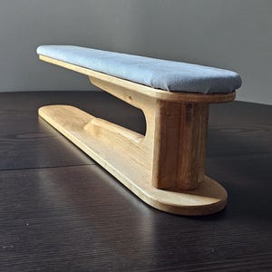 Könnte beinhalten: Ein hölzernes Ärmelbrett mit einem hellblau gepolsterten Oberteil. Das Brett besteht aus hellfarbigem Holz und hat einen gebogenen Sockel. Das gepolsterte Oberteil ist rechteckig und scheint aus einem weichen Stoff zu bestehen. Das Brett ist zum Bügeln von Ärmeln bestimmt.