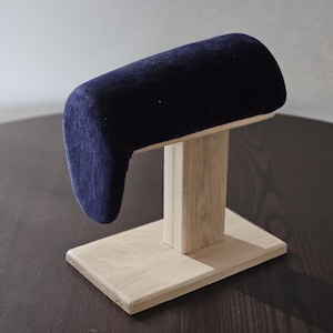 Könnte beinhalten: Ein Hutständer aus Holz mit einem blauen Samtkissen. Der Ständer hat einen rechteckigen Sockel und einen vertikalen Pfosten, der das Kissen trägt.
