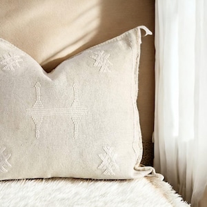 May include: A white throw pillow with a geometric pattern embroidered on the front. The pillow is made of a soft, textured fabric.