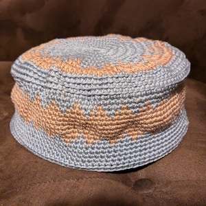 Könnte beinhalten: Eine gehäkelte Mütze mit einem blauen und braunen Muster. Die Mütze ist aus einem strukturierten Garn gefertigt und hat eine abgerundete Krone.