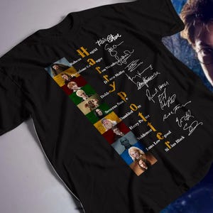 Könnte beinhalten: Schwarzes T-Shirt mit den Worten "Harry Potter" in Gold und Weiß, begleitet von Charakterbildern und Unterschriften. Das Shirt zeigt Bilder von Charakteren wie Dumbledore und Voldemort. Im Hintergrund ist ein Porträt von Harry Potter zu sehen.