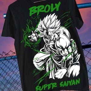 May include: A black short-sleeved t-shirt featuring a white graphic illustration of the character Broly in a dynamic pose. The design includes green energy effects and the text BROLY and SUPER SAIYAN printed in green capital letters on the front.