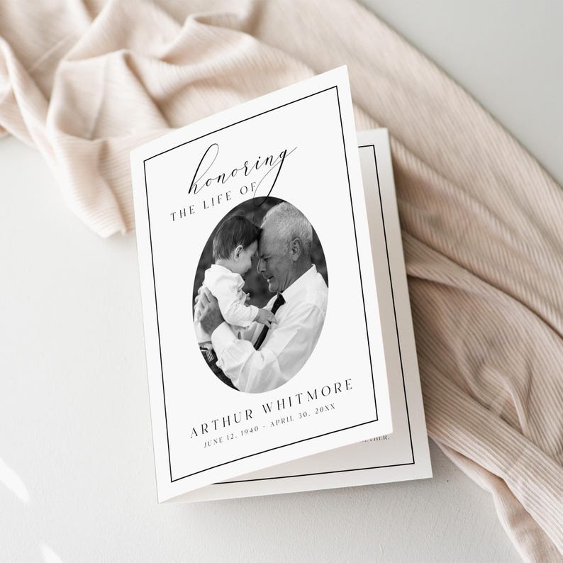 Puede incluir: Una tarjeta conmemorativa blanca con un borde negro, con el texto "Honoring the Life Of" en escritura. Una foto ovalada en blanco y negro muestra a un hombre sosteniendo a un beb&eacute;. El nombre "Arthur Whitmore" y las fechas est&aacute;n debajo.