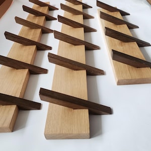 Op de afbeelding: Een set van drie houten wandbevestigde kapstokken met schuine, donkerbruine houten haken. De kapstokken zijn gemaakt van licht hout en hebben een natuurlijke afwerking.