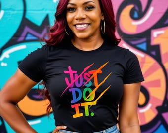 May include: A black t-shirt with the text "Just Do It" in a rainbow gradient. The shirt is worn by a person with red hair and hoop earrings, posing in front of a colorful graffiti wall. The person is wearing blue jeans.