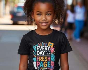 Può includere: T-shirt nera con la scritta "EVERY DAY IS A FRESH PAGE" in colori vivaci. Il design include illustrazioni di articoli scolastici come matite, quaderni e uno zaino. La t-shirt è indossata da una bambina.