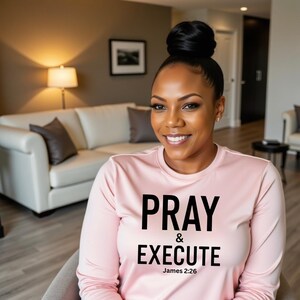 May include: A woman wearing a pink long-sleeved shirt with the text "Pray & Execute James 2:26" printed on the front.