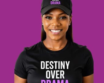 May include: A black baseball cap and t-shirt with the text "DESTINY OVER DRAMA" in white and purple. The cap is worn on the head, and the t-shirt is on the upper body. The background is a solid purple color.