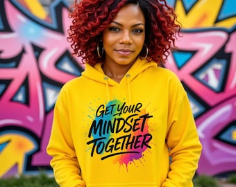 May include: A yellow hoodie with the text "GET YOUR MINDSET TOGETHER" in black, with a colorful paint splatter design. The person in the image has red curly hair and is wearing gold hoop earrings.