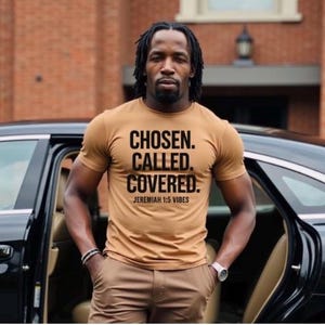 May include: A man wearing a brown t-shirt with the text "CHOSEN. CALLED. COVERED. JEREMIAH 1:5 VIBES" printed on it.