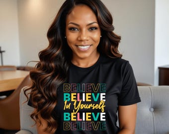 May include: Black t-shirt with the words "BELIEVE In Yourself BELIEVE BELIEVE" in a colorful, stacked design. The shirt is worn by a person with long, wavy brown hair.