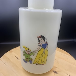 May include: A cylindrical white glass lamp shade featuring a colourful graphic of Snow White and Dopey holding hands. Snow White wears a blue bodice and yellow skirt, while Dopey is dressed in a green tunic with a yellow hat and purple shoes.