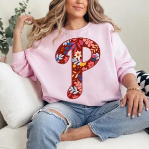 May include: A pink sweatshirt with a floral patterned letter "P" on the front.