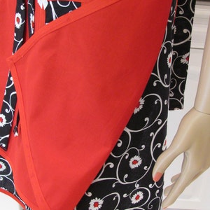 May include: Red and black apron with a floral pattern. The apron has a large pocket on the front and a tie at the neck.