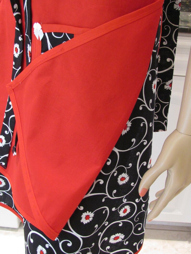 May include: Red and black apron with a floral pattern. The apron has a large pocket on the front and a tie at the neck.