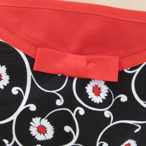 May include: Black and white fabric with a red bow and a floral pattern. The fabric has a red trim around the top.