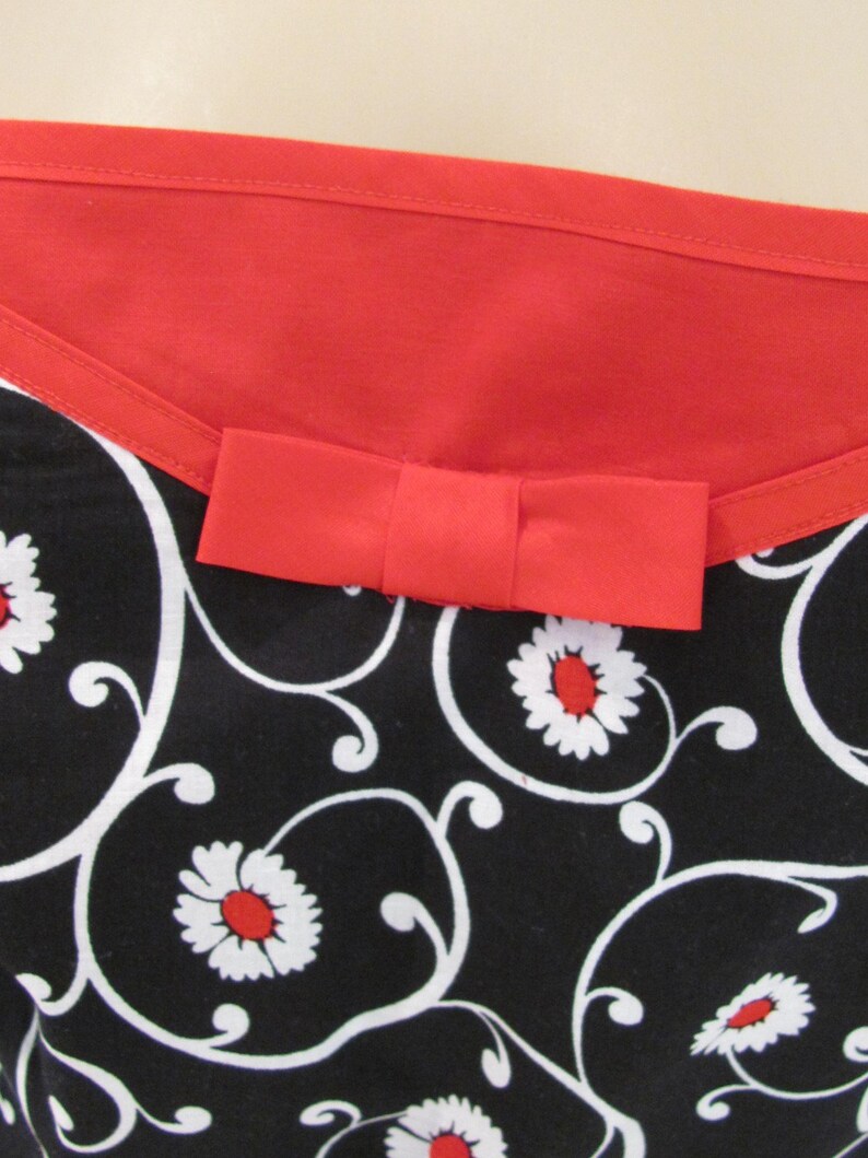 May include: Black and white fabric with a red bow and a floral pattern. The fabric has a red trim around the top.