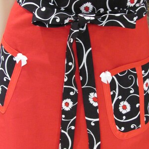 May include: Red apron with black and white floral print. The apron has a tie waist and two pockets.