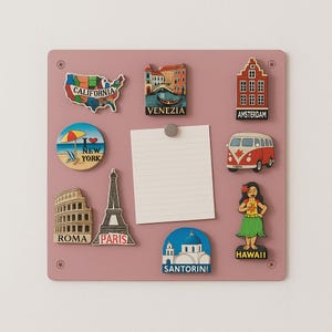 May include: A pink magnetic board displaying travel-themed magnets. Magnets include a map of California, a Venice scene, an Amsterdam building, a New York beach scene, a red and white van, a Roman Colosseum, the Eiffel Tower, a Santorini scene, and a Hawaiian hula dancer.